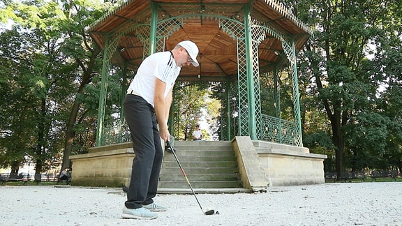 Ein Mann  steht mit Golfschläger vor einem Pavillon.