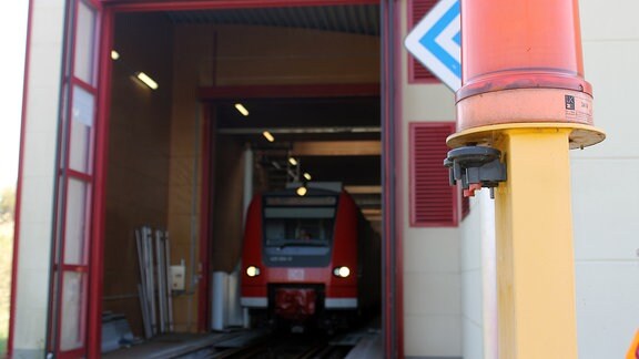 ein roter Zug fährt aus einer Halle heraus