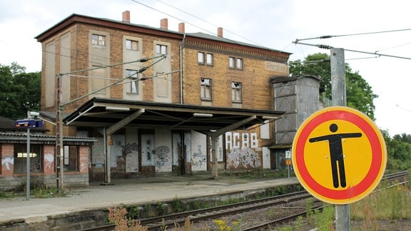 Ein Schild weist darauf hin, dass der Durchgang verboten ist, im Hintergrund ein dreigeschossiges Bahnhofsgebäude.