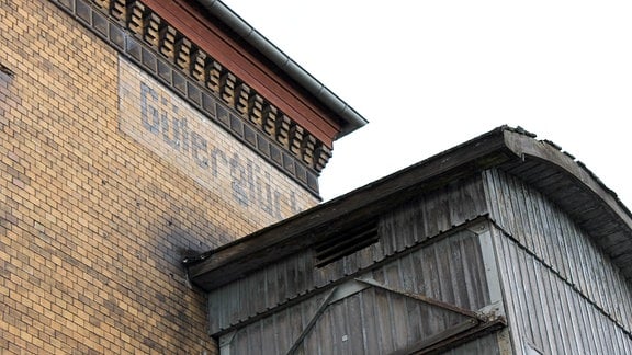 Blasser Schriftzug „Güterglück“ unter der Dachkante eines Bahnhofsgebäudes.