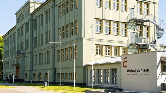 Ein großes Gebäude, daneben weist ein Schild auf die Hochschule Anhalt in Köthen hin.