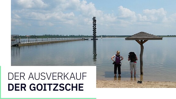 Zwei Personen stehen am Ufer des Goitzsche-Sees und blicken auf den Pegelturm.