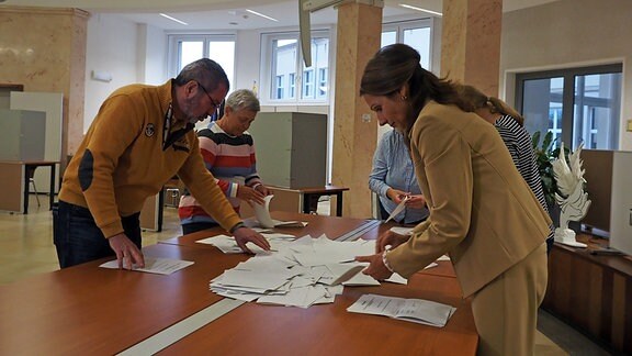 Fünf Menschen stehen um einen Tisch und zählen Stimmzettel aus.