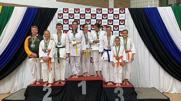 Mehrere Karate-Kämpfer stehen mit Medaillen auf einem Siegertreppchen bei den Weltmeisterschaften in Südafrika 2019.