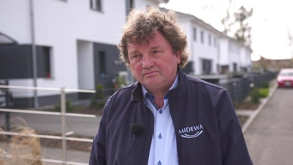 Midewa-Chef Uwe Störzner im MDR-Interview, hinter ihm sind vier Doppelhäuser des Wohngebiets "Zur Luther Linde" in Muldenstein zu sehen.