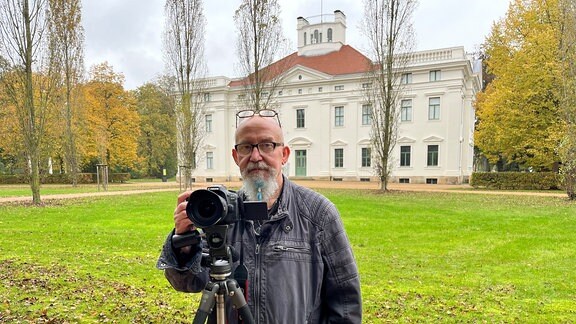 Frank Fiedler, ein Mann mit Bart und Brille steht hinter einem Kamerastativ im Dessauer Park