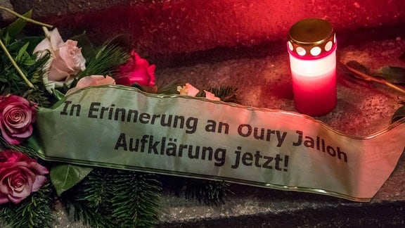 In Erinnewrung an Oury Jalloh Aufklärung jetzt steht auf einem Band, daneben Blumen und eine Kerze