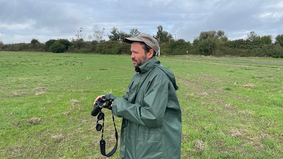 René Köhler steht mit Fernglas auf einem Feld im Zerbster Land. Er leitet das Wideransiedlungsprogramm von Großtrappen in Anhalt-Bitterfeld.