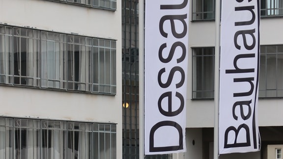 Vor dem Bauhaus Dessau stehen weiße Fahnen mit der Aufschrift "Dessau" und "Bauhaus"