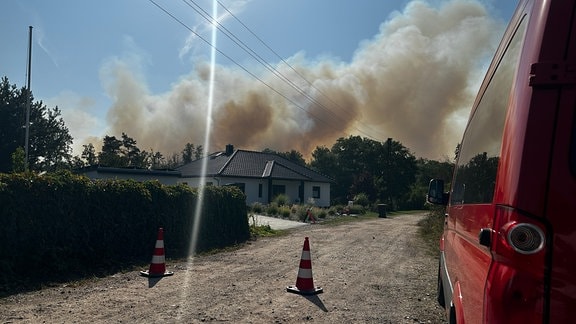 In der Stadt Oranienbaum-Wörlitz im Landkreis Wittenberg tobt ein Waldbrand und Rauchwolken sind hinter einem Wohnhaus zu sehen. 