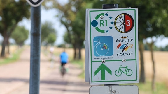 Ein grün umrandetes Schild weist auf mehrere Fahrradrouten hin, die alle demselben Weg folgen