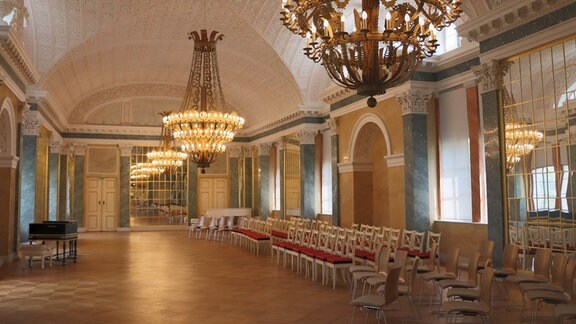 Blick in den Spiegelsaal des Köthener Schlosses, drei Stuhlreihen stehen unterhalb der drei Kronleuchter