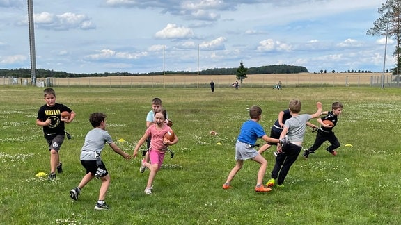 Kinder spielen zusammen Football auf Wiese.