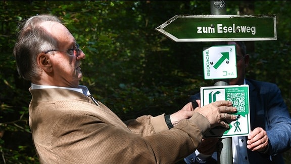 Rainer Haseloff (CDU), Ministerpräsident von Sachsen-Anhalt, bringt ein neues Schild am Lutherweg an.