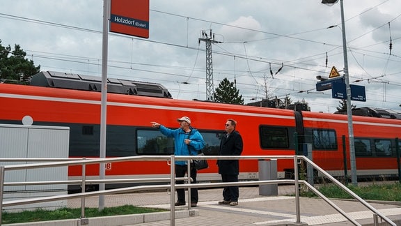 Zwei Männer stehen am Bahnsteig in Holzdorf.