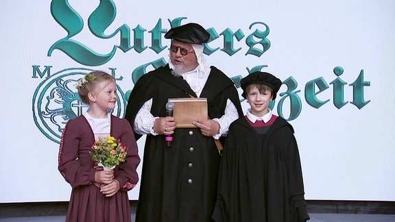 Zwei Kinder und ein Erwachsener stellen die Hochzeit Luthers nach.