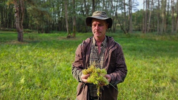 Ein Mann mit Hut steht in der Dübener Heide und hält Gras in der Hand. 