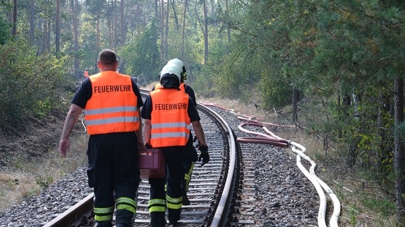 Feuerwehrkräfte tragen während eines Waldbrandes in der Oranienbaumer Heide Geräte entlang einer alten Eisenbahnstecke.