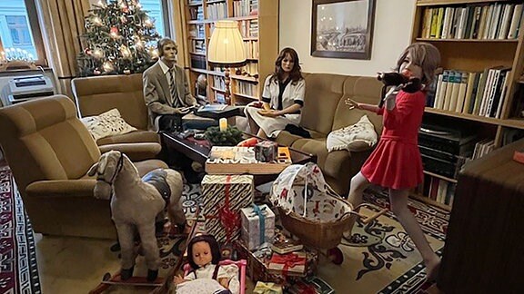 In einem Museum ist ein Wohnzimmer im weihnachtlichen Stile der 1920er Jahre dekoriert. Darin sitzen Puppen.