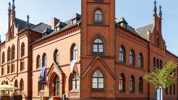 Rotes Backsteingebäude mit zahlreichen Fenstern und Spitzbögen, darin ist das Rathaus von Zahna-Elster im Landkreis Wittenberg untergebracht