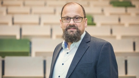 Daniel Bachmann, Prof. Hochschule Magdeburg-Stendal. Mann mit Brille und Bart steht vor einer Wand.