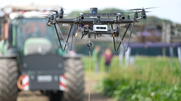 Eine Drohne schwebt bei einer Technikschau auf einem Feld in Nordsachsen vor einem Traktor mit Düngevorrichtung.