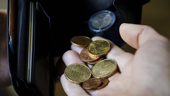 Cent Münzen werden in ein Portemonnaie geschüttet.