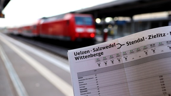 Ein Fahrplan von Salzwedel und Wittenberg über Stendal nach Magdeburg wird vor einen roten Regionalzug gehalten