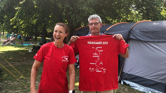 Zwei Menschen mit roten T-Shirts stehen vor einem Zelt