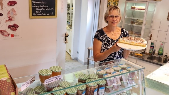 Frau Schuster präsentiert im Café der Schäferei Schuster eine selbstgebackene Torte.