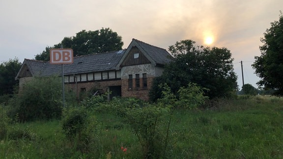 Ein verfallenes Bahnhofsgebäude in Harpe mit einem großen DB Schild davor.
