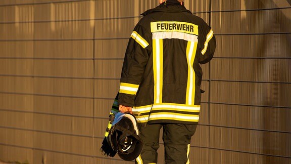Ein Feuerwehrmann im Feuerwehranzug einem Helm in der Hand