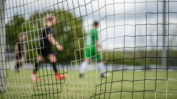 Spielerinnen sind während eines Fußballspiels hinter einem Netz eines Tors zu sehen.