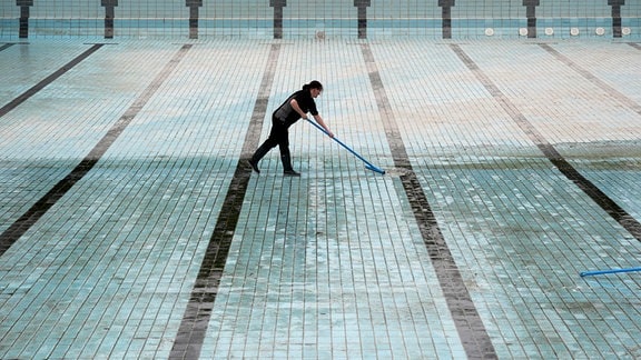 Eine Mitarbeiterin einer Reinigungsfirma reinigt das große Becken Freibad. 