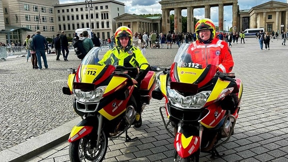 Zwei Männer auf rot-gelben Motorrädern vor dem Brandenburger Tor in Berlin