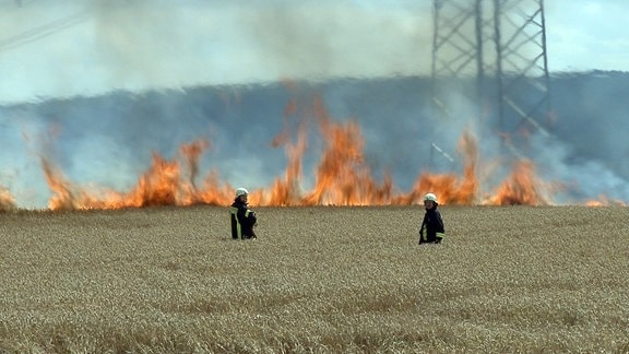 Zwei Feuerwehrmänner vor einem brennenden Feld