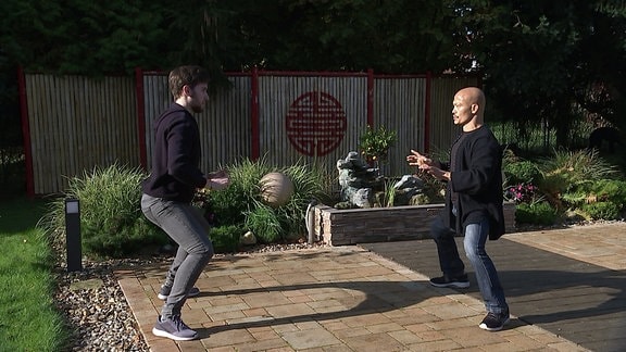 Zwei Männer in dunkler Kleidung machen Kung-Fu-Übungen auf einer Gartenterrasse