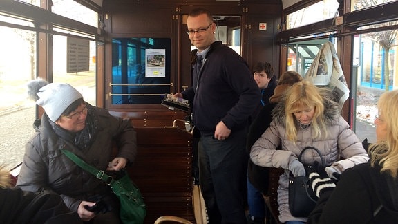 Mehrere Fahrgäste einer historischen Straßenbahn in Naumburg werden von einem Schaffner kontrolliert