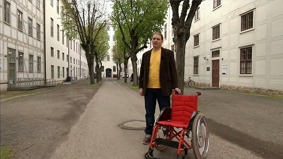 Ein Mann steht im Hof der Franckeschen Stiftungen in Halle. Neben ihm steht ein roter Rollstuhl