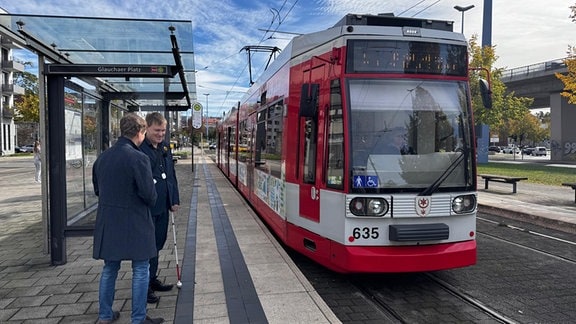 Zwei Männer stehen an einer Straßenbahnhaltestelle in Halle