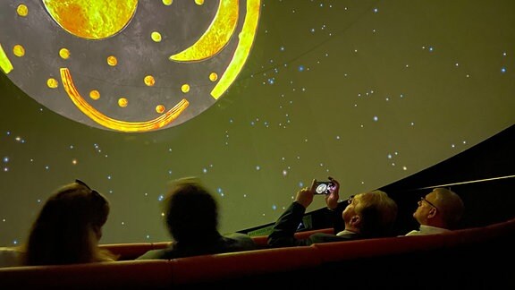 Vier Personen schauen sich in einem Planetarium den Nachthimmel mit der Himmelsscheibe von Nebra an.