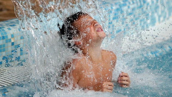 Ein Kind unter einem Wasserfall in einem Schwimmbad.