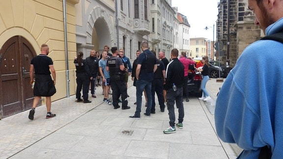 Ein paar Polizisten stehen beim CSD 2023 an einer Zugangsstraße zum Marktplatz von Weißenfels Menschen gegenüber.