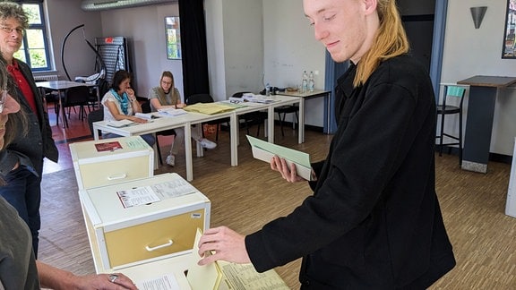 Ein junger Mann und Wahlhelfer in einem Wahllokal.