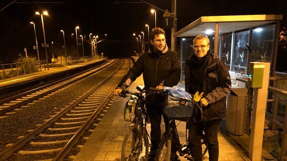 Leonard Schubert und André Plaul stehen in der Dunkelheit mit Fahrrädern an einem Bahngleis