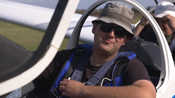 Ein junger Mann mit Sonnenbrille sitzt im Cockpit eines Segelfliegers.