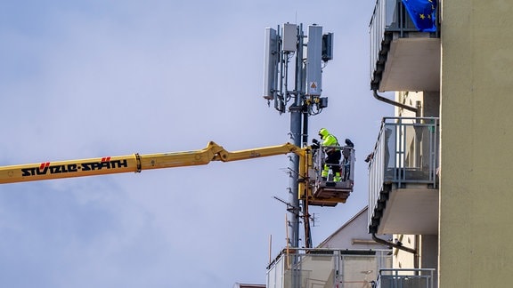 Arbeiter in einem Krankorb montieren auf dem Dach eines Wohnhauses einen Mobilfunkmast.