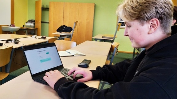 Ein Schüler sitzt in einem Klassenraum vor einem Laptop