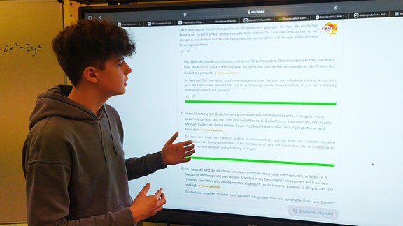 Ein Schüler steht an einem großen Smartboard und erklärt etwas.