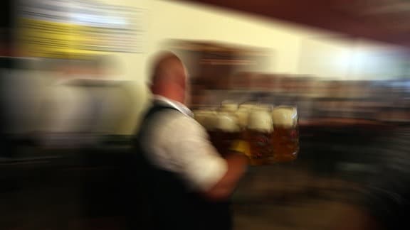 Ein Kellner trägt mehrere Maß Bier zu den Gästen.